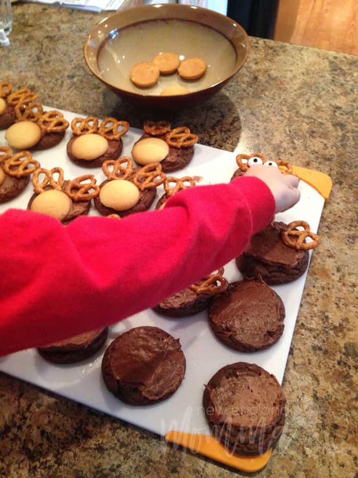 chocolate cookies being decorating with cookie wafers and pretzels by a toddler boy
