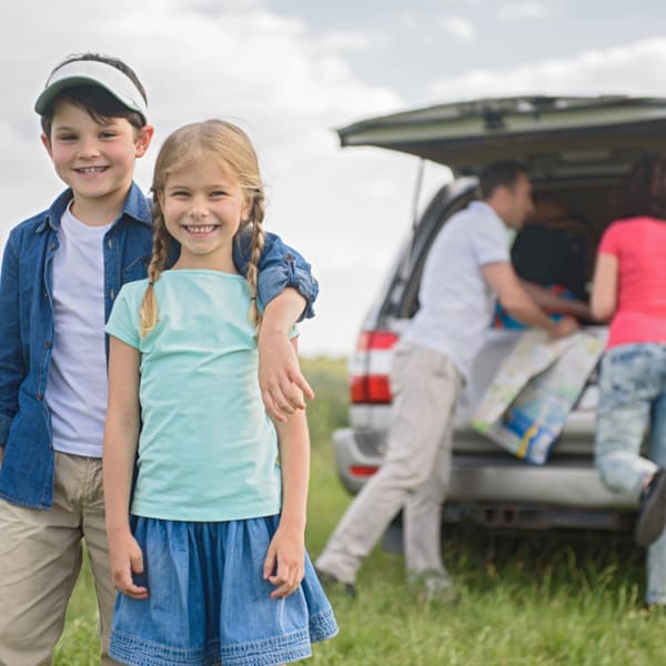 Mom, dad packing up the car while a boy and girl wait and smile