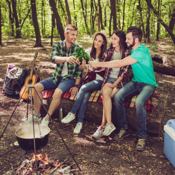 Four adults with at a campfire with drinks outside.