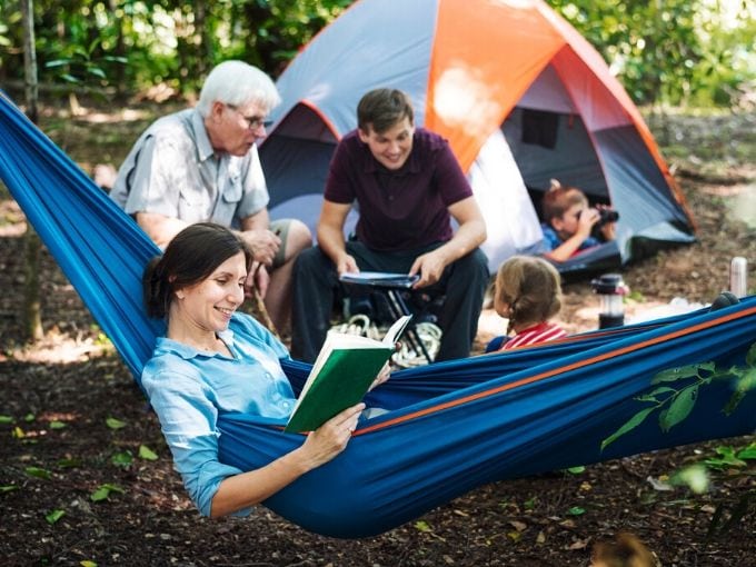 mom in a hammock reading a book with family around tent in campsite