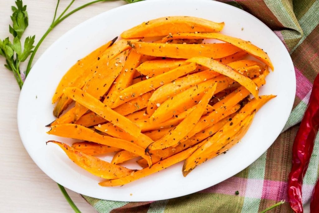 a white plate with roasted sweet potato fries and seasoning