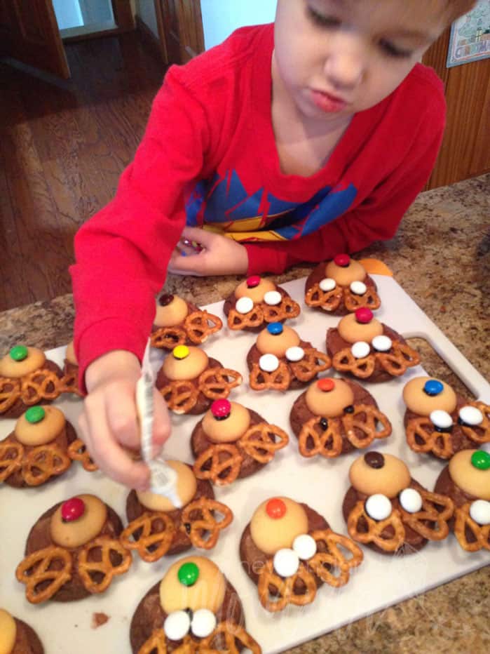 Toddler decorating cookies into reindeers with cookie wafers, pretzels and M&Ms.