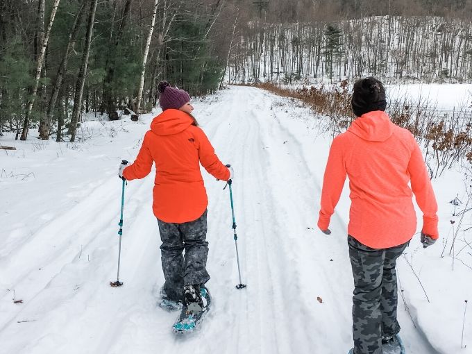 two moms snowshoeing on a trail next to the woods 