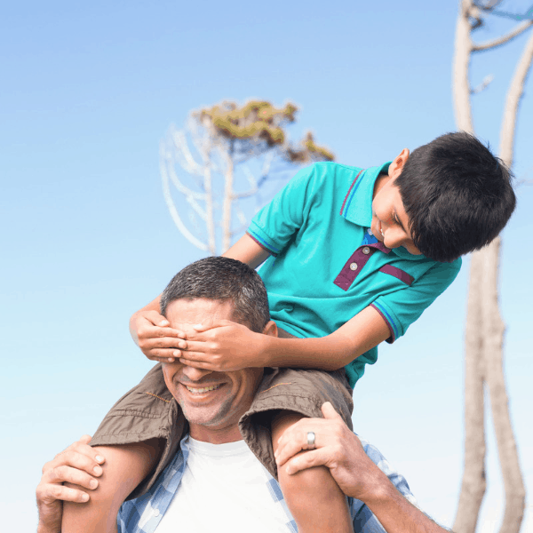 A dad with his young son on his shoulders happy outside. 