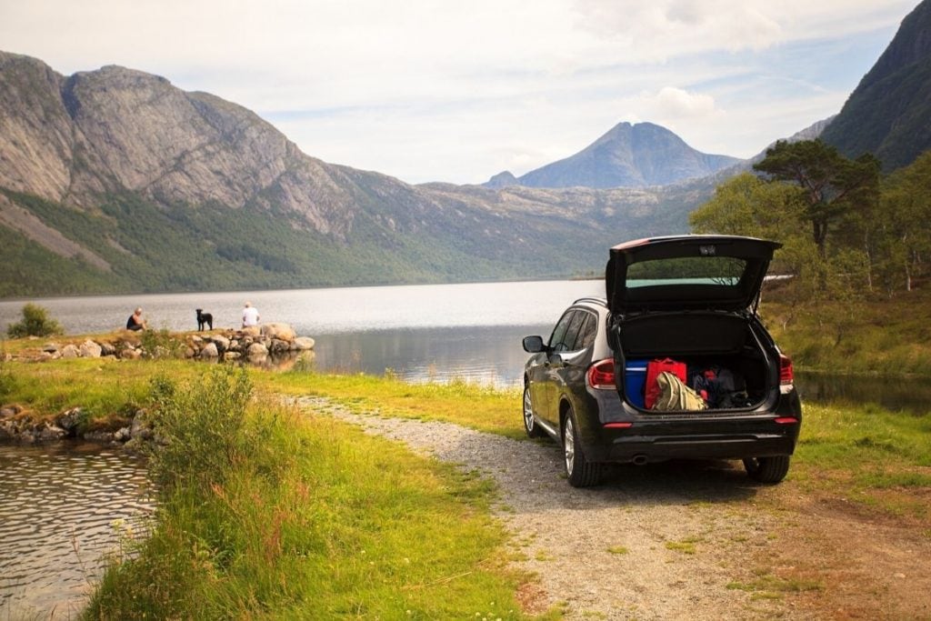 A car parked at a lake while the family rests in the grass