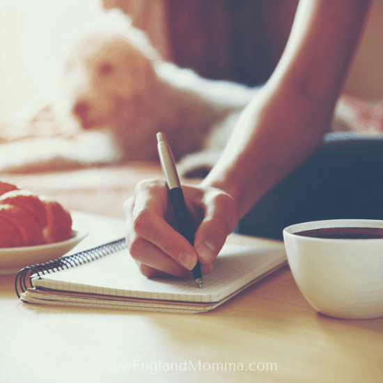 A woman relaxing while writing in journal with coffee and dog nearby 