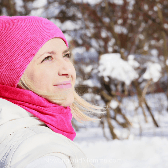 A woman dressed in a pink hat and scarf outdoors soaking in the sun on her face