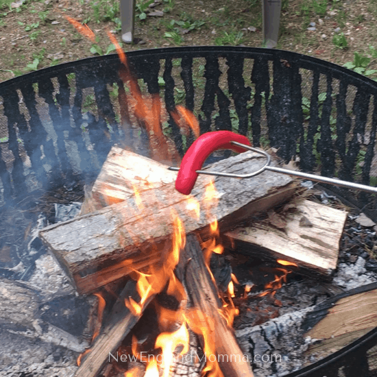 a red hot dog on a metal fork over a campfire. 