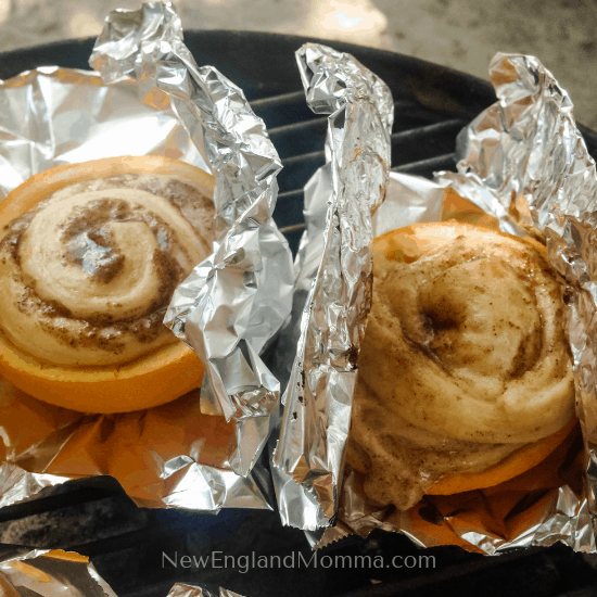2 cinnamon rolls baking up in oranges in tin foil