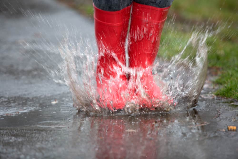 Child's red boots splashing in the rain puddles while camping