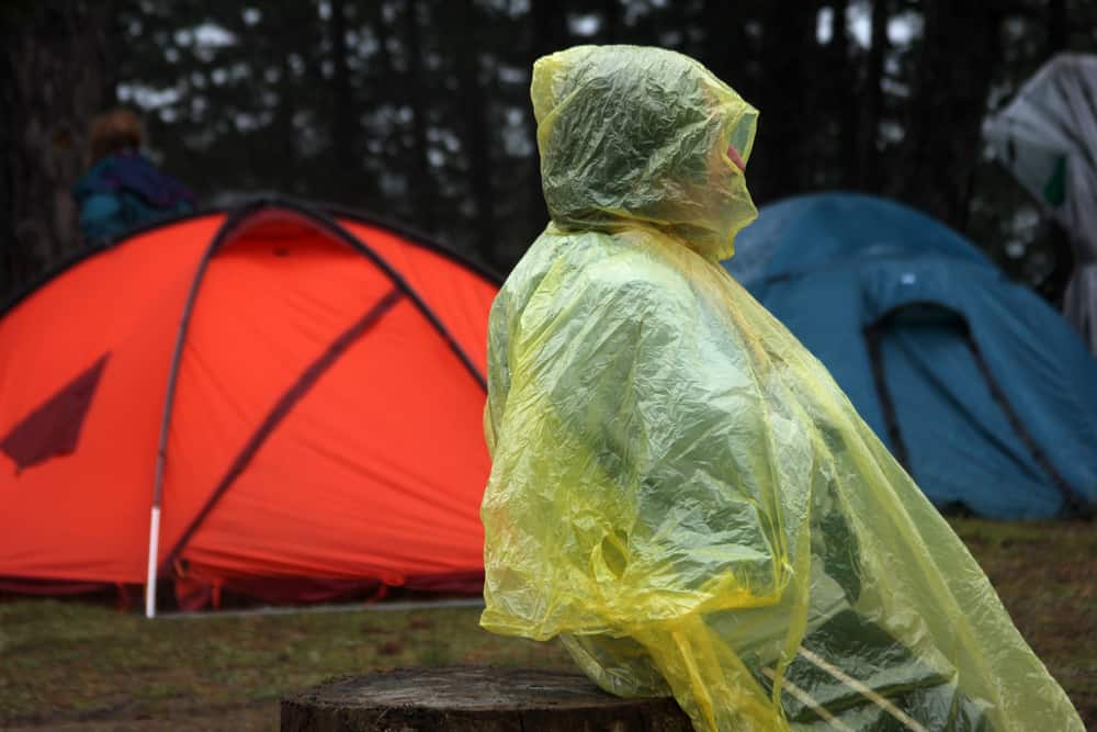 A camper in a rain poncho by a couple of tents waiting out the wet weather