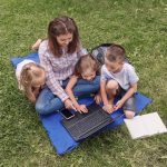 mom and kids outdoors on a laptop planning a day trip