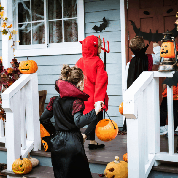 Kids in costumes trick or treating at a home with a decorated front porch