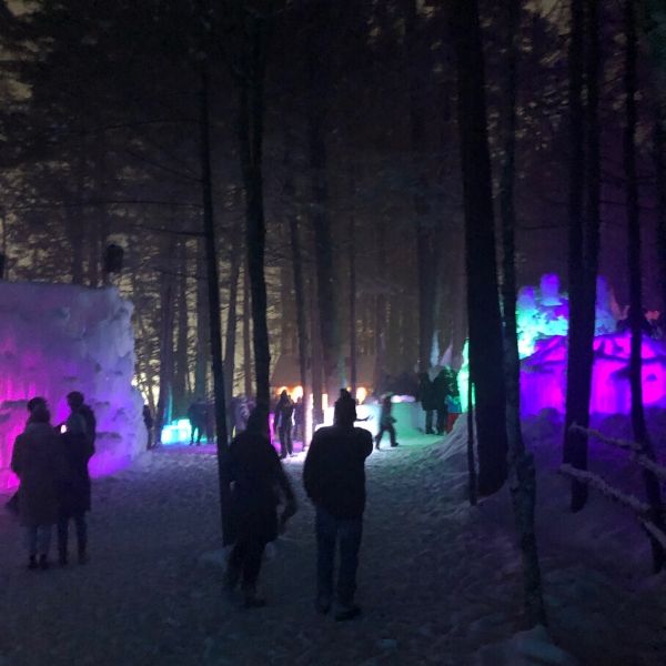 People walking around at night with colorful lit up ice walls at Ice Castles. 