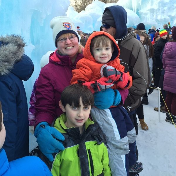 A mom and two boys dressed in warm winter clothes waiting in line at the Ice Castles