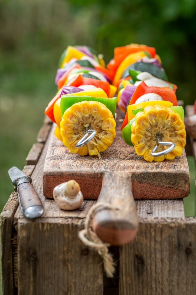 a variety of cut up vegetables on skewers outdoors on a cutting board