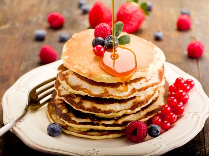 a stack of 5 pancakes with various berries and maple syrup with a fork 