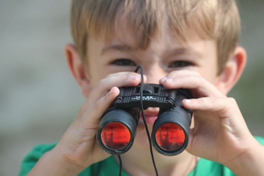 young boy looking through binoculars wearing a green shirt