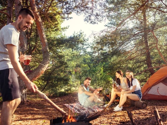 2 guys and 2 woman at a campfire enjoying beers 