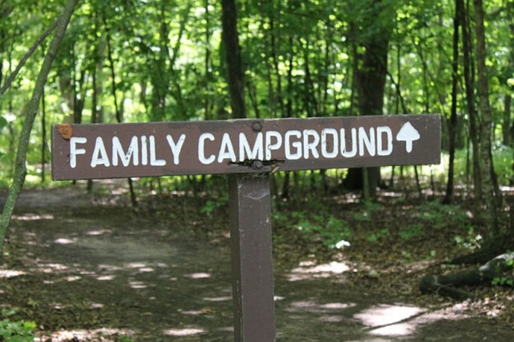 a brown wooden sign with white painted letters spellign out Family Campground with an arrow in the woods. 