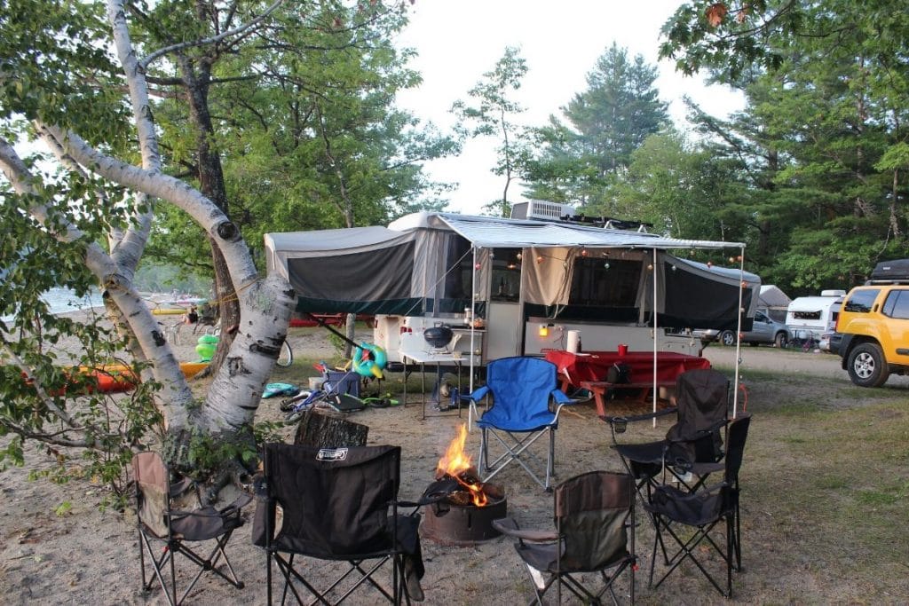 a pop up trailer with a campfire and camp chairs around it. 