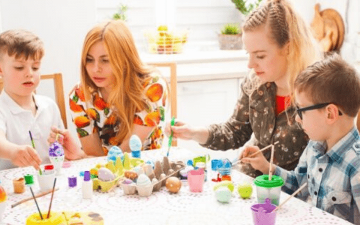 two moms and two boys decorating Easter eggs at a table with paint