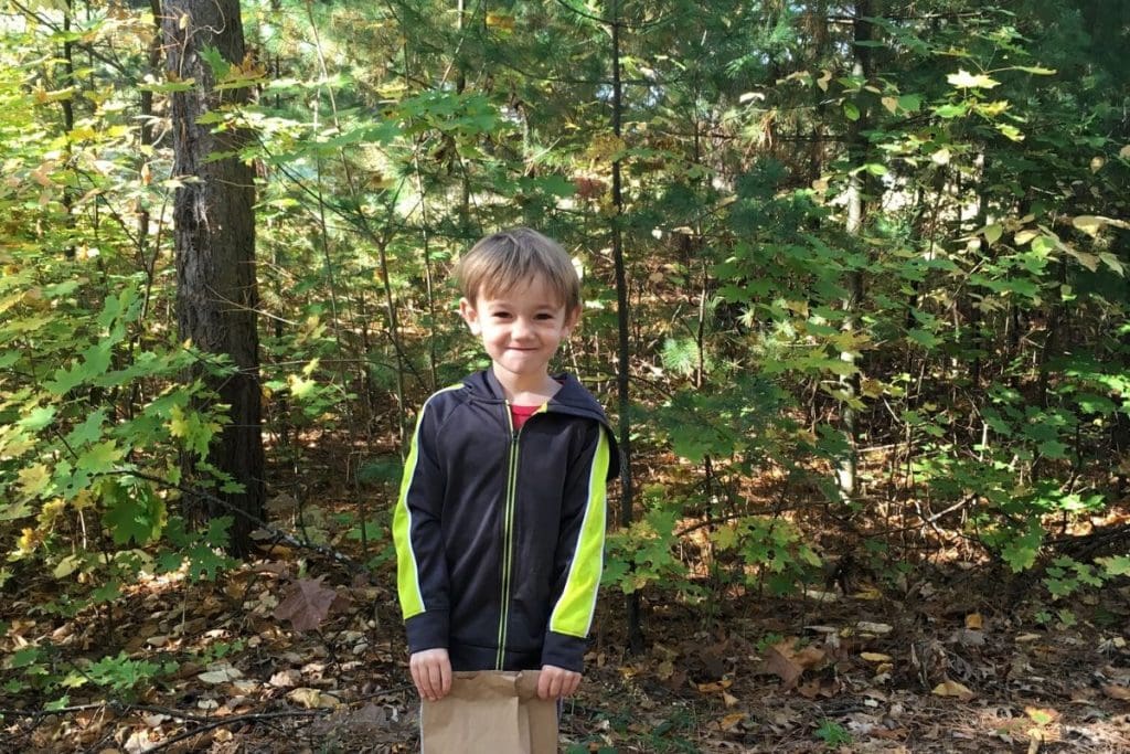 young boy on a hike with a brown paper bag in the woods to collect nature treasure