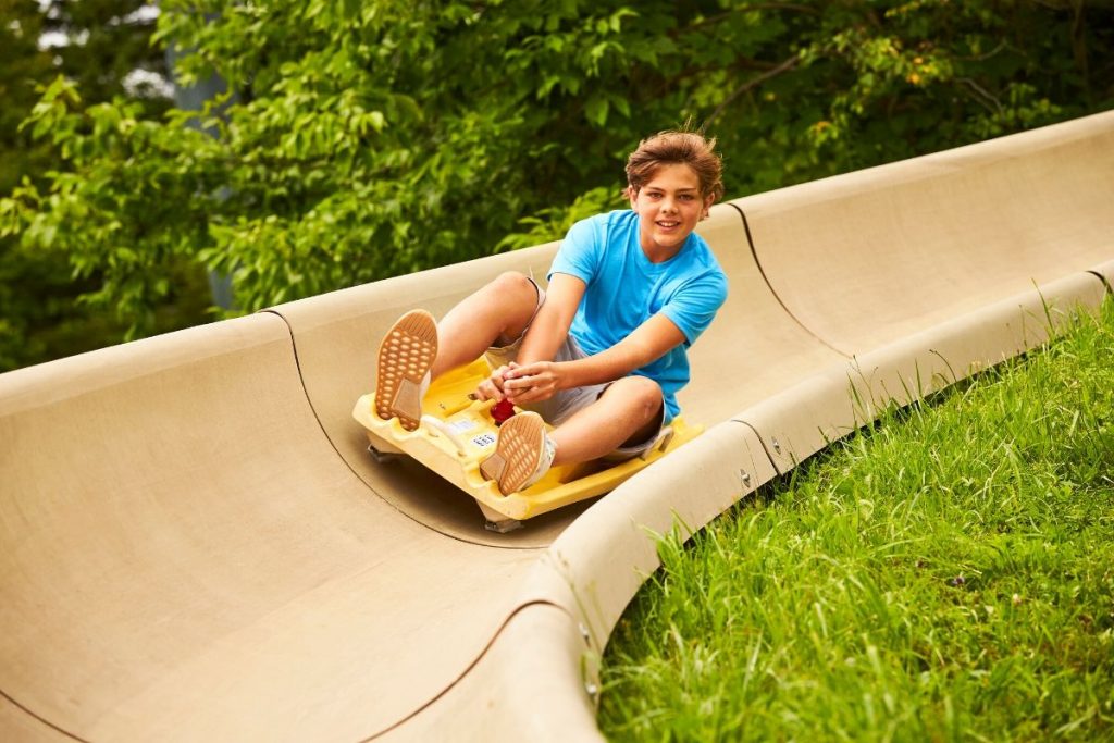 A teen boy smiling as he zooms down a mountain coaster in the summer time