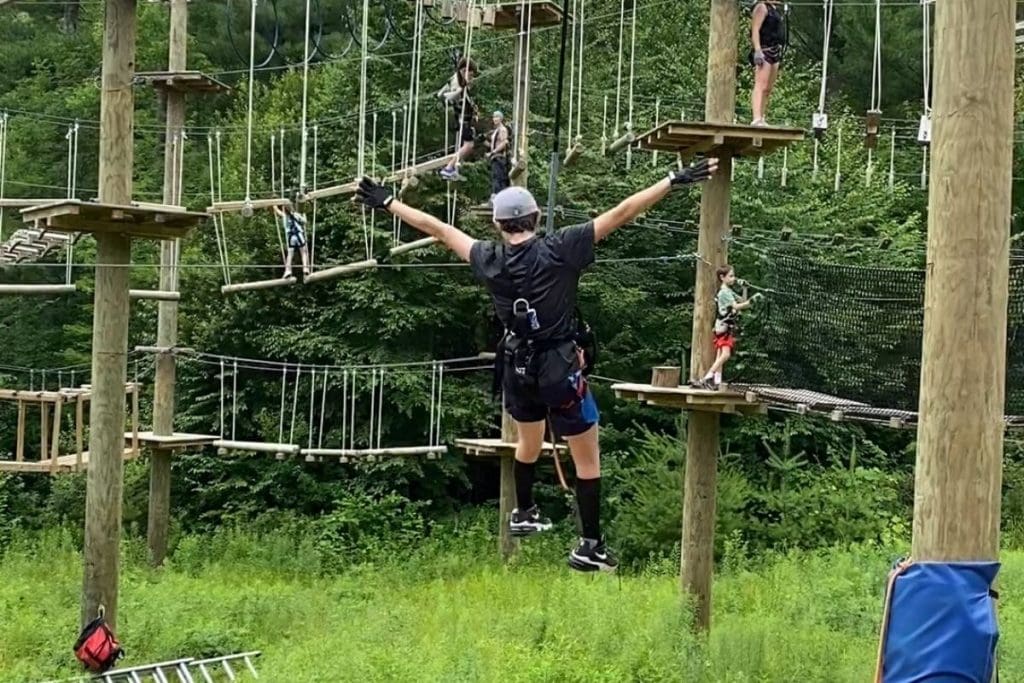 A teenager on an aerial rope course with his arms out as he zip lines down from a platform