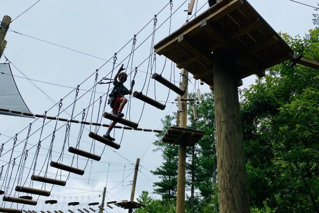 A young boy on an aerial rope course high over head climbing up higher to a platform