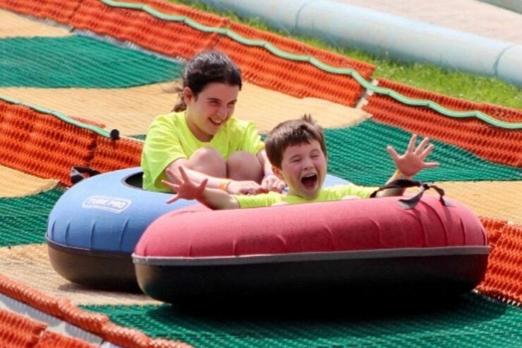 Two happy kids yelling as they zoom down in an inner tube 