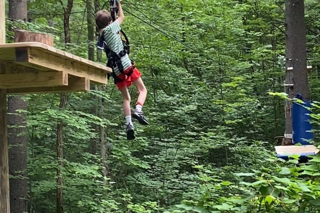 An 8-year old boy on a zip line aerial obstacle through the trees at Boundless Adventures Berlin MA