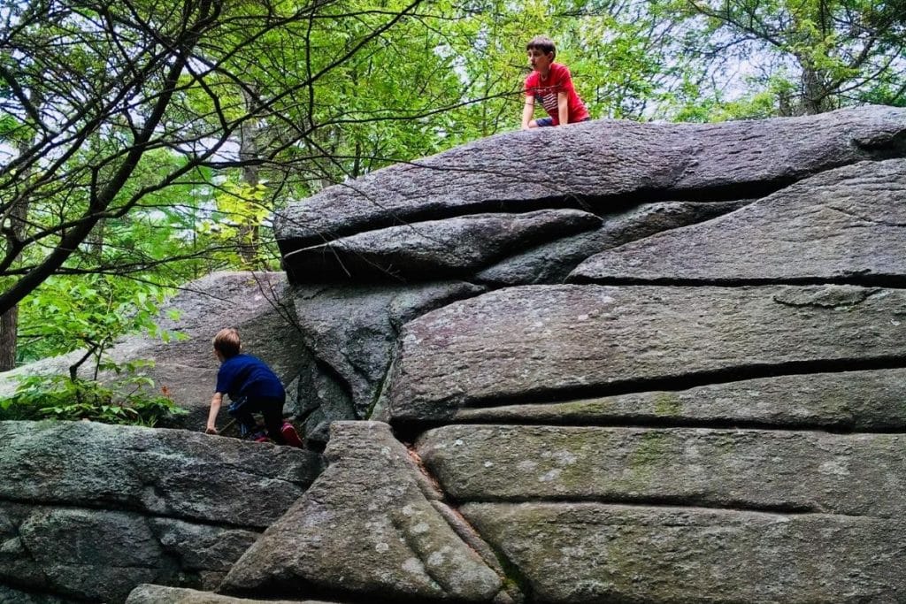 Two boys climbing up a huge boulder 