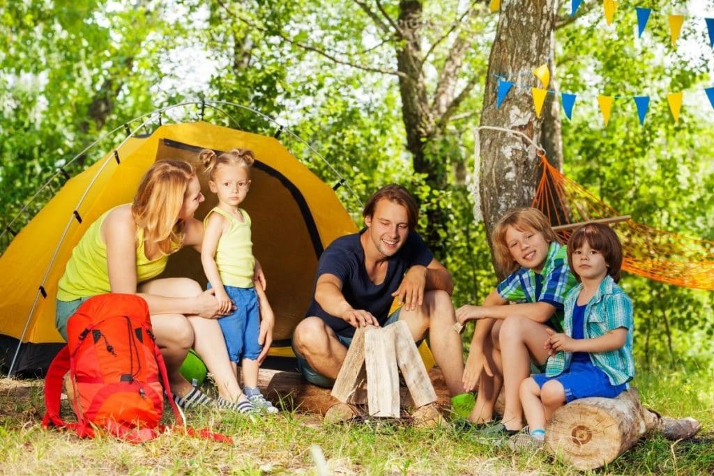 Parents and 3 kids outside a tent camping outdoors and smiling 
