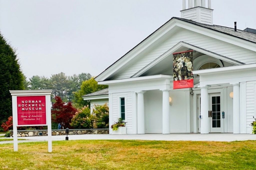 Small house-like structure of the Norman Rockwell Museum with a red sign out front on a fall day in Stockbridge