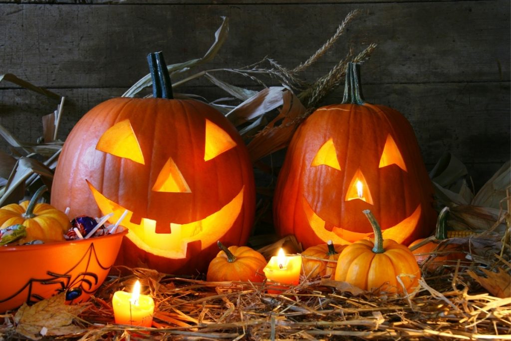 two lit up jack-o-lanterns on straw set up for Halloween