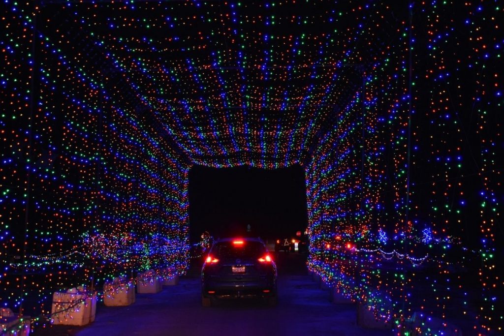 A car driving through a festive holiday light tunnel during the Christmas season.