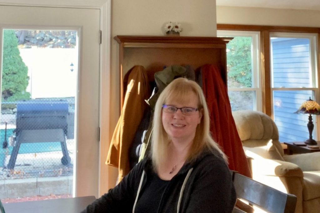 A woman in her home sitting down and smiling 