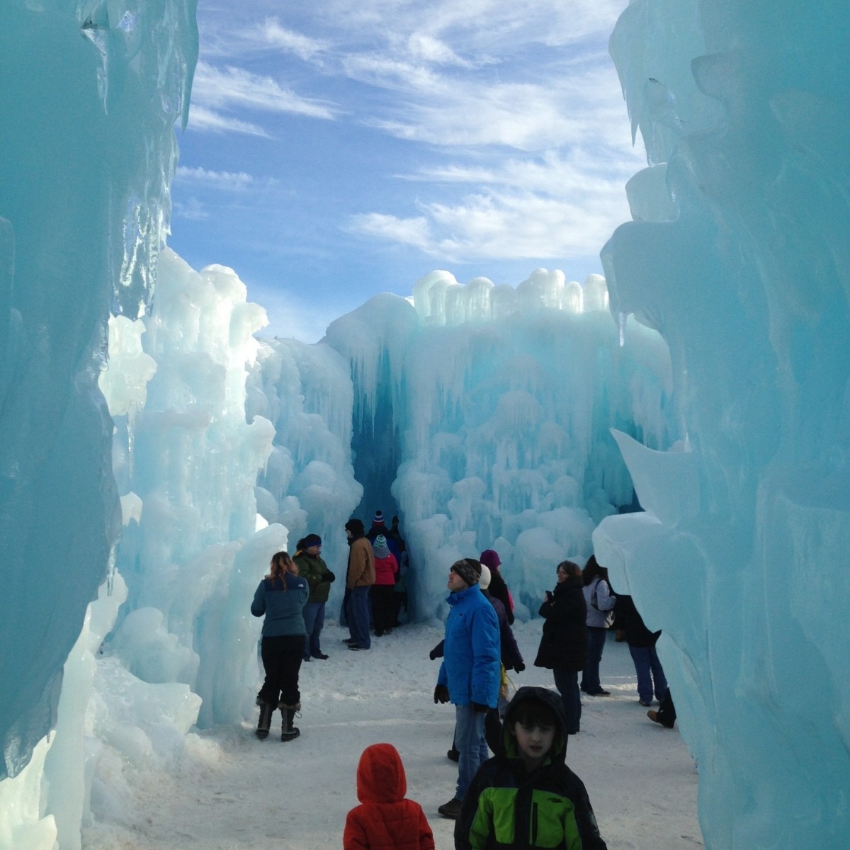 Tall walls of ice at the Ice Castles in New Hampshire with people walking around. 